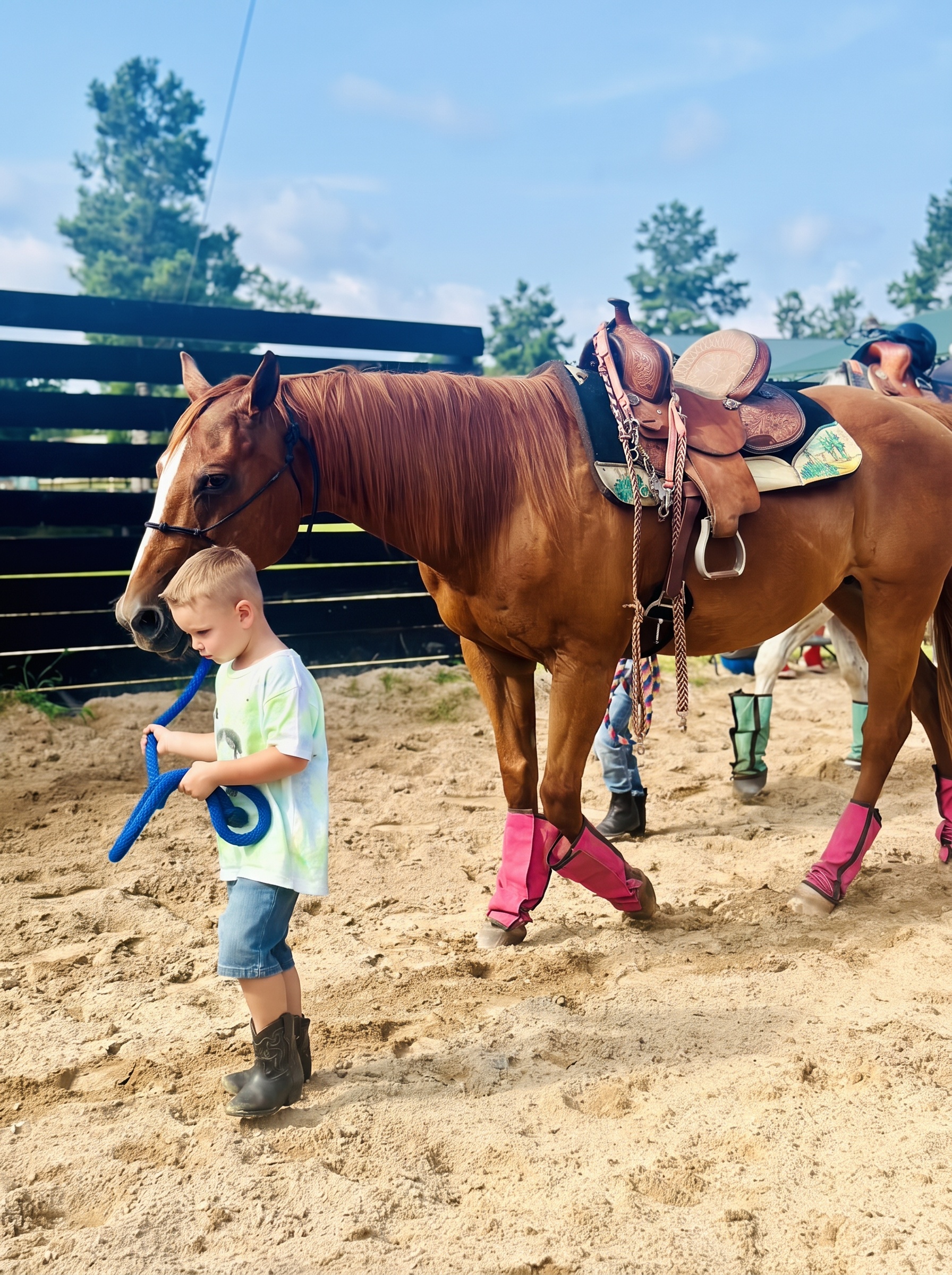 A toddler in cowboy boots leading a gentle chestnut horse by a blue rope